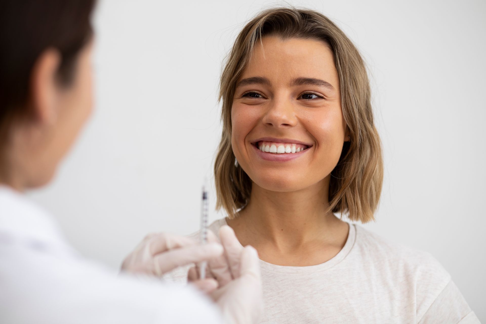 Woman smiles at doctor holding syringe in a white room.