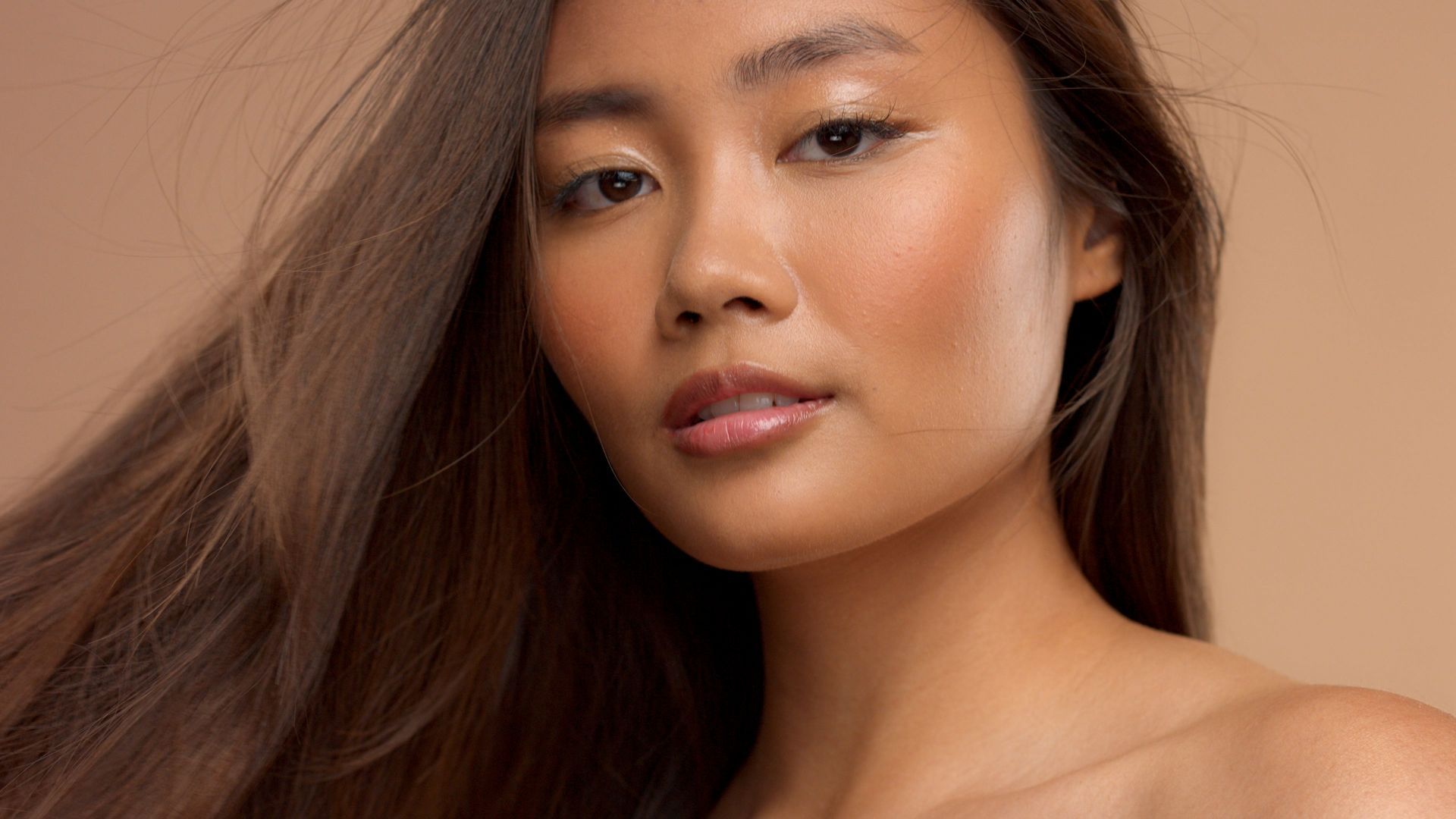 A close up of a woman 's face with long hair blowing in the wind.