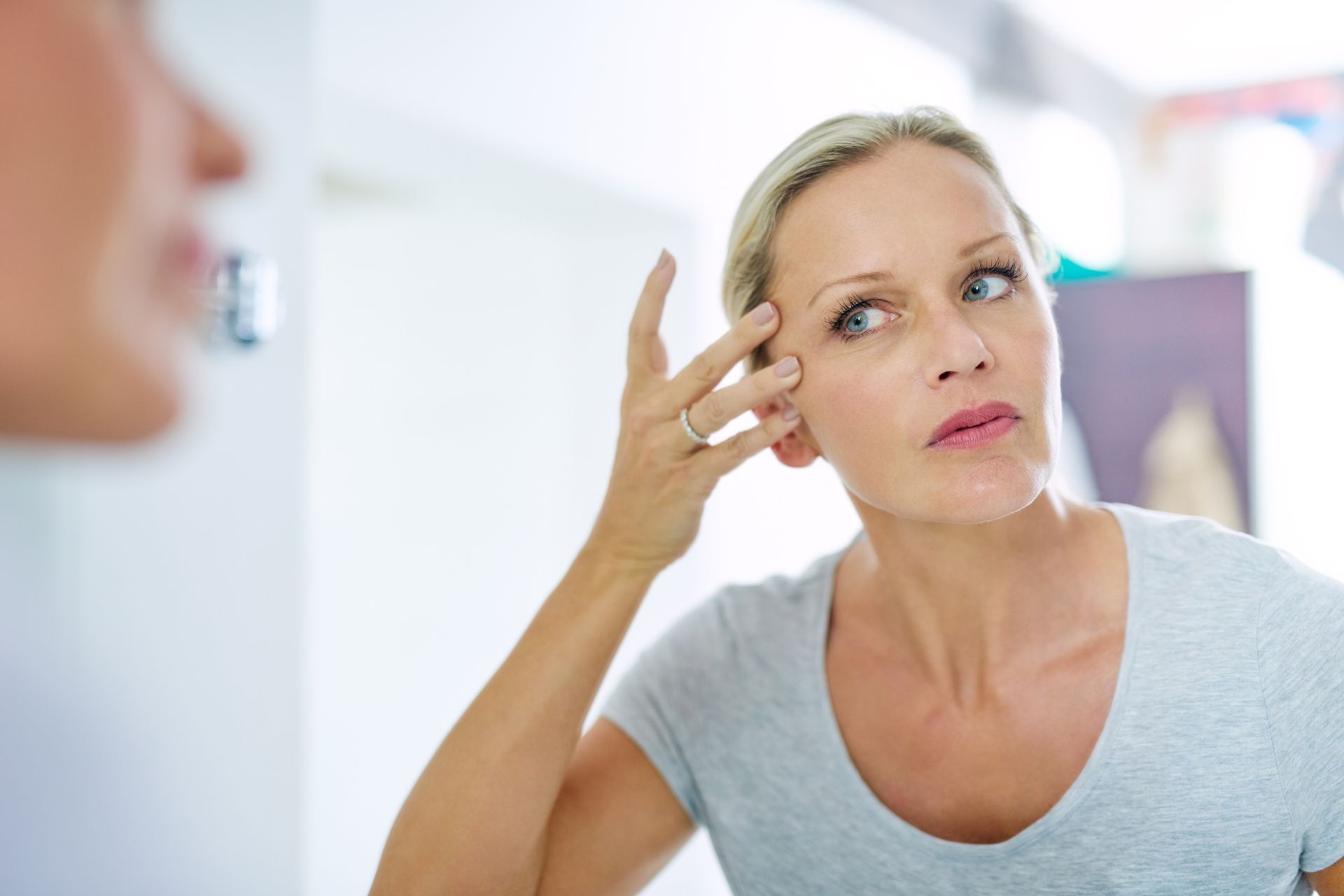 A woman is looking at her face in the mirror.