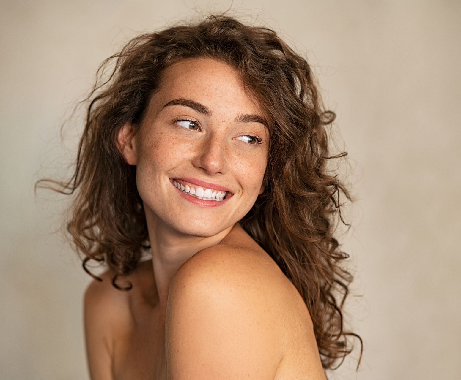 A woman with curly hair is smiling and looking over her shoulder.