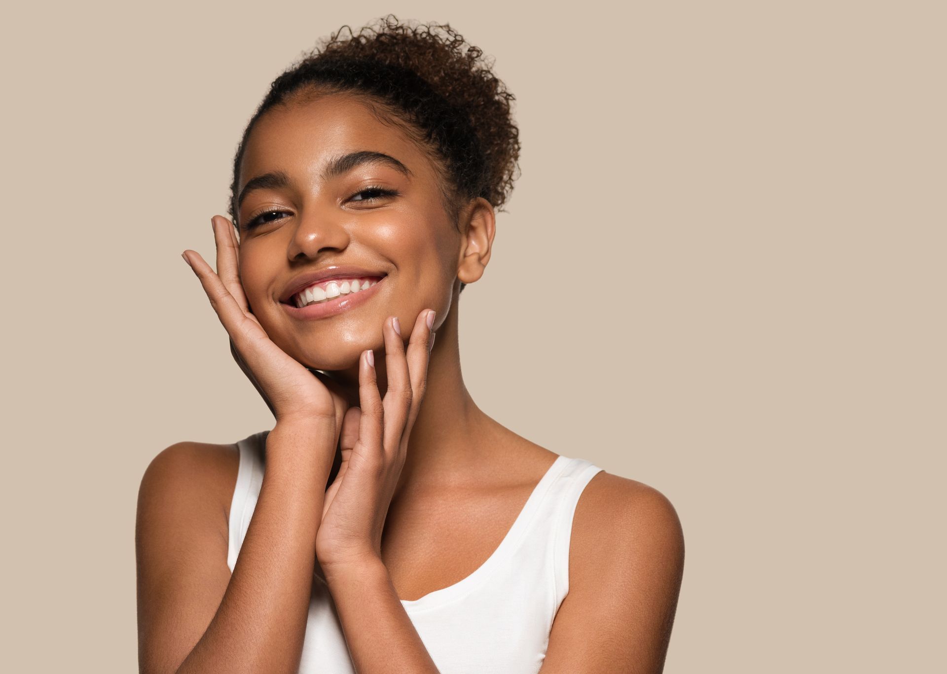 A woman is smiling and touching her face with her hands.