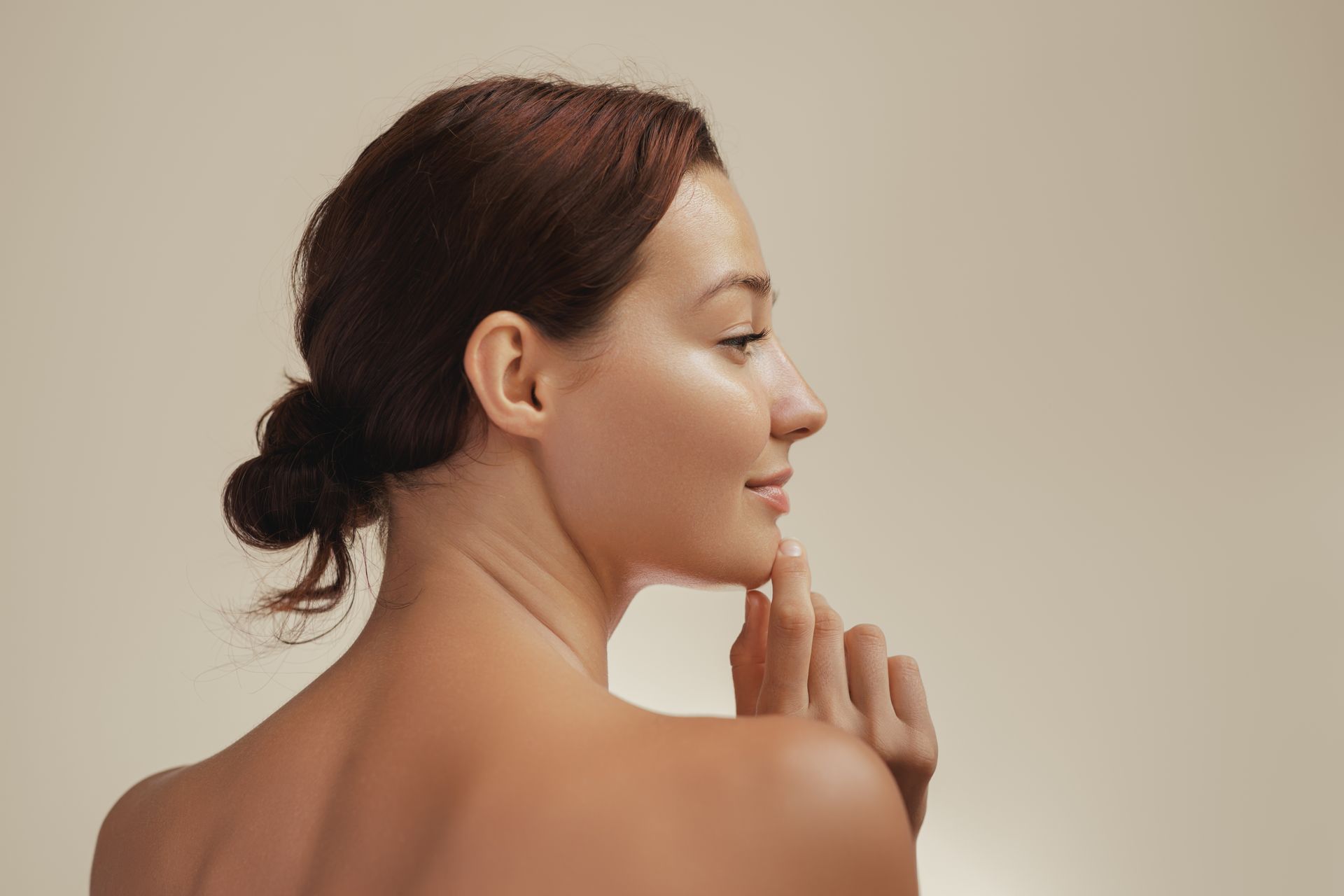 A woman is touching her face with her hand and looking over her shoulder.