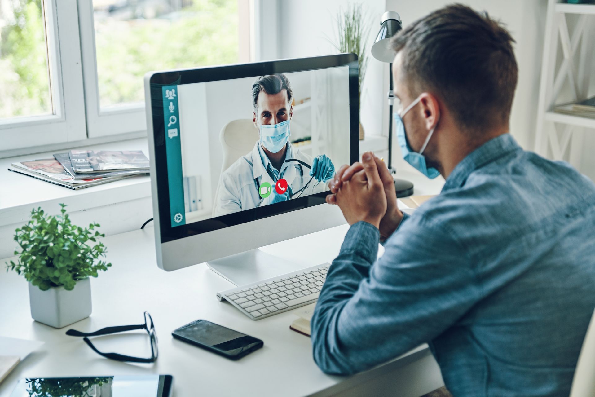 A man wearing a mask is having a video call with a doctor on a computer.