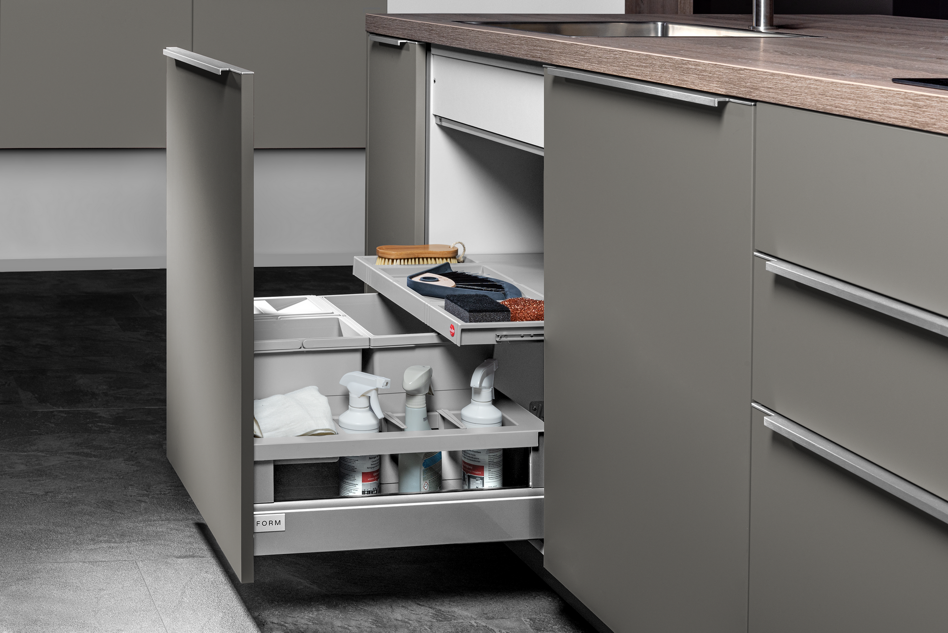 A cabinet with pull-out drawers in a modern kitchen. The drawers hold cleaning supplies.