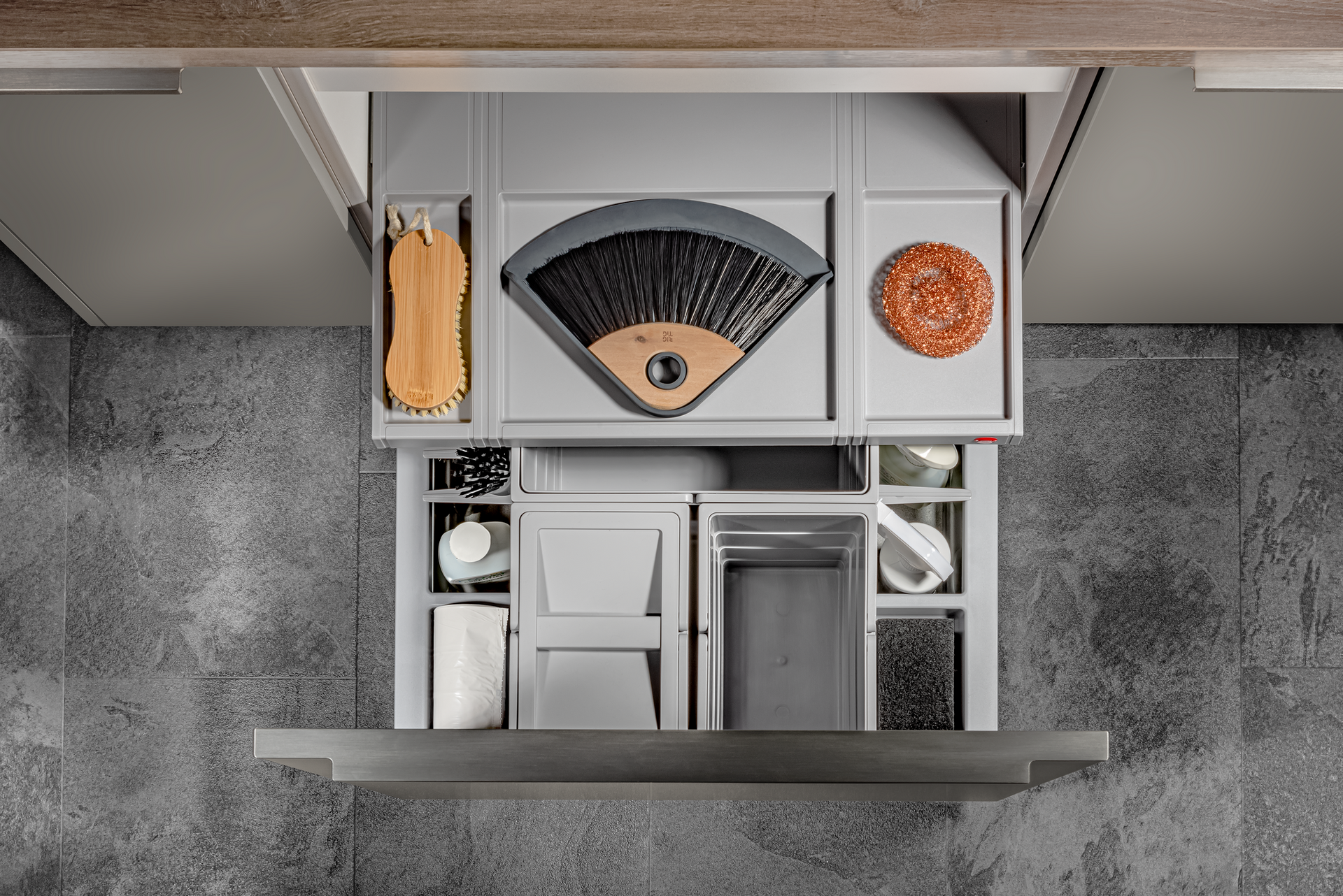 Overhead view of a hidden kitchen vent with compartments holding kitchen tools and ingredients. Gray-toned with textured wall background.