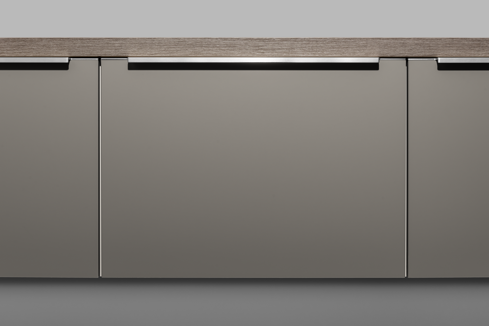 Close-up of modern kitchen cabinets in a neutral gray with integrated metal handles. A wooden countertop is above.