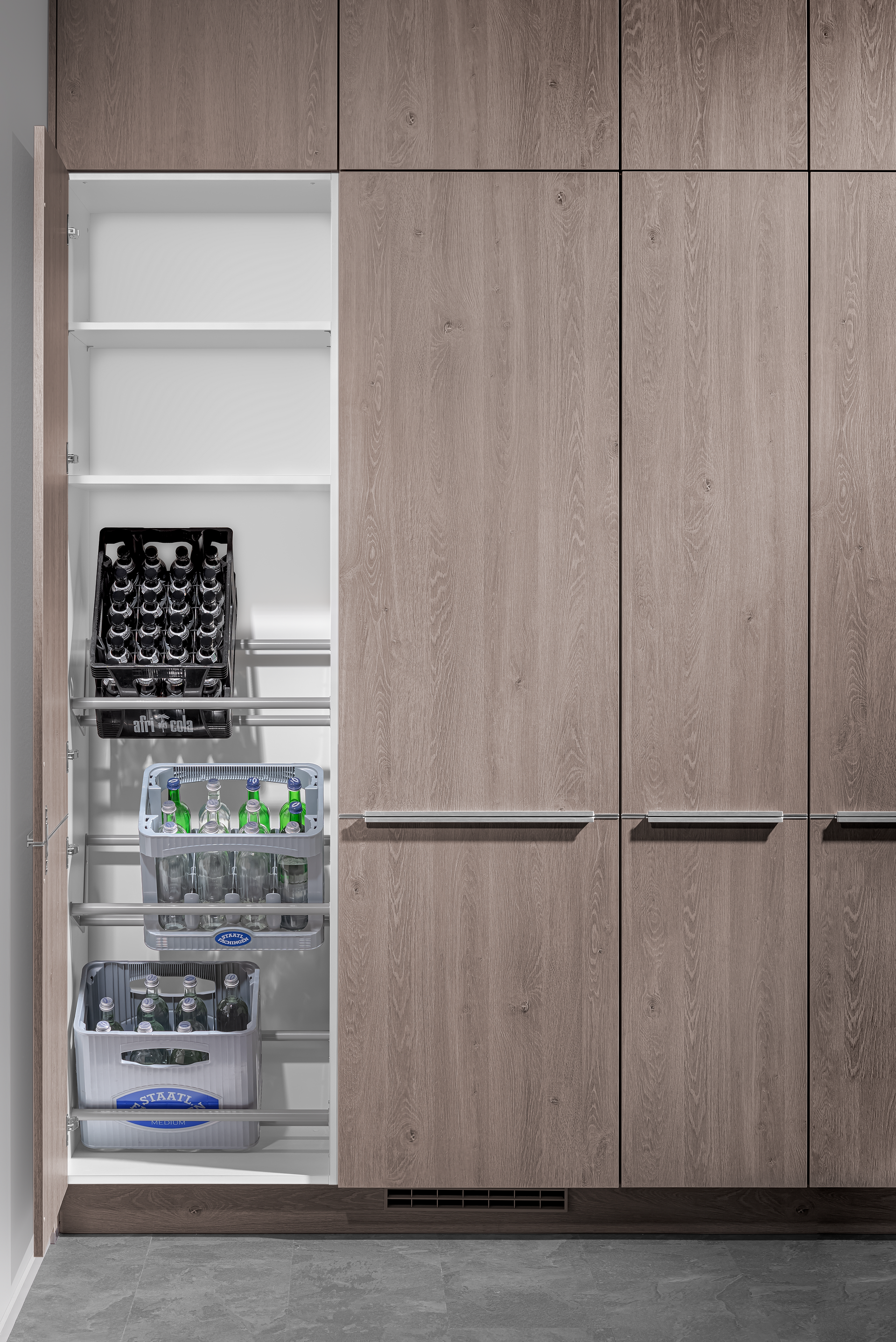 Tall pantry cabinet with pull-out shelving filled with beverages, open to reveal white interior. Exterior is textured, wood-look finish.