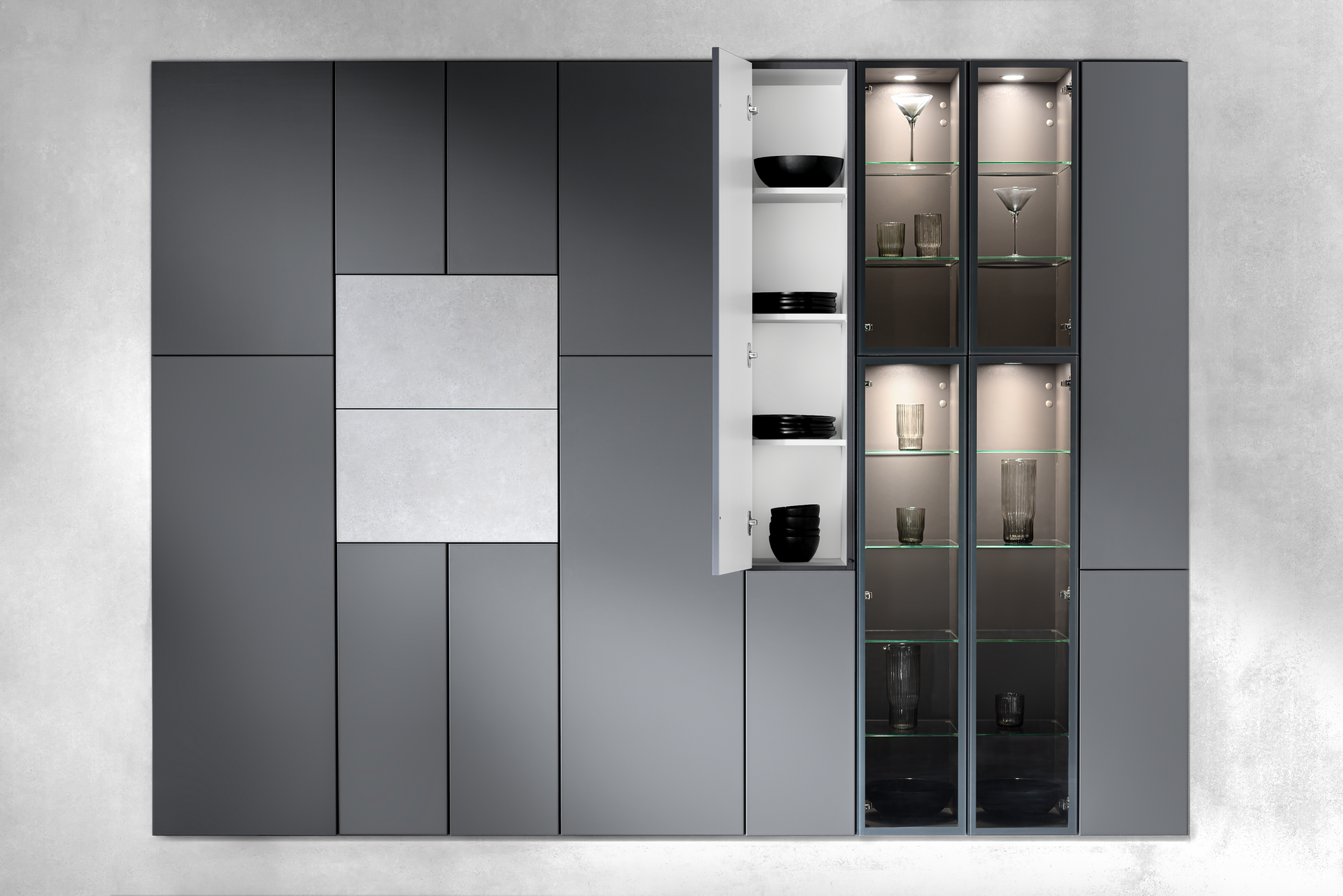 Modern gray wall-mounted storage cabinets with one open, revealing shelves and built-in lighting, and glass display cases with illuminated glassware.