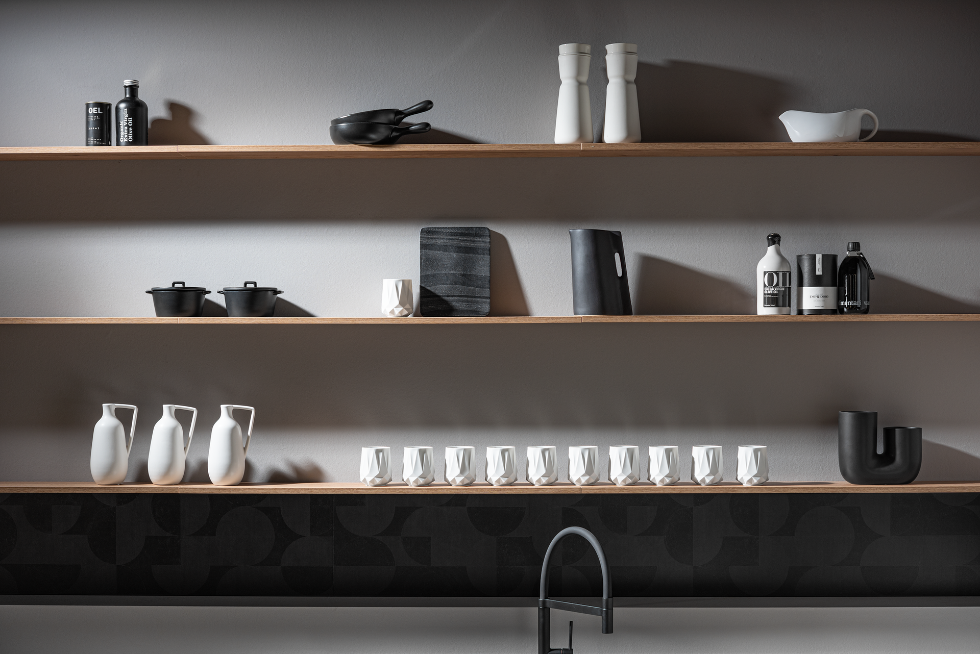 Kitchen shelves stocked with black and white items, including jars, bottles, and a salt and pepper set, with a faucet below.