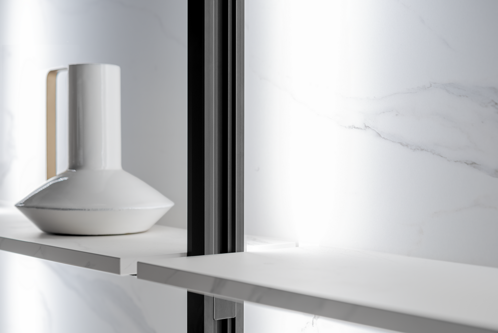 White vase on a light shelf, part of a modern shelving unit against a marbled wall.