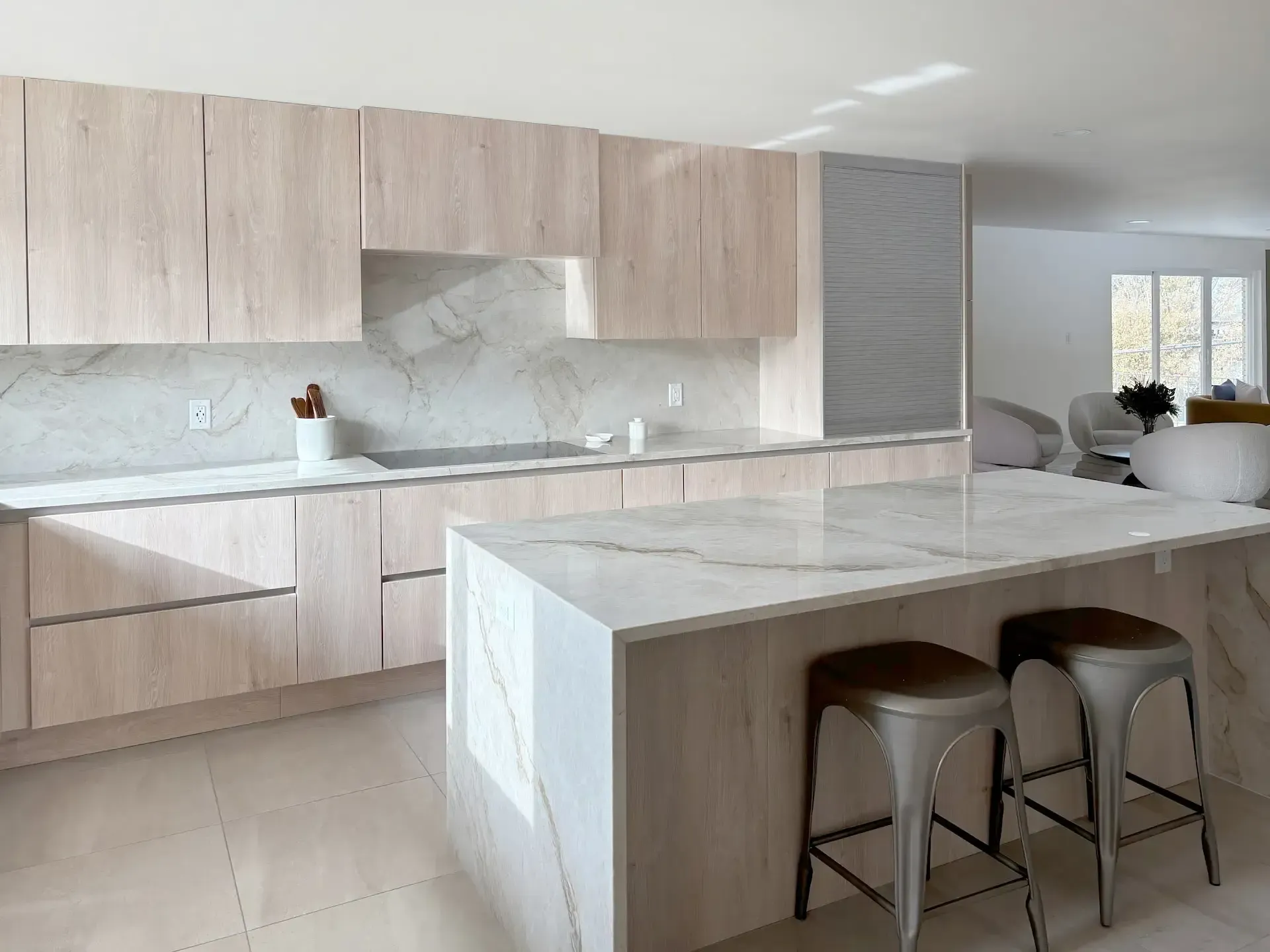 Modern kitchen with light wood cabinets, marble countertops, and two bar stools at an island. Modern kitchen with light wood cabinets, marble countertops, and two bar stools at an island.