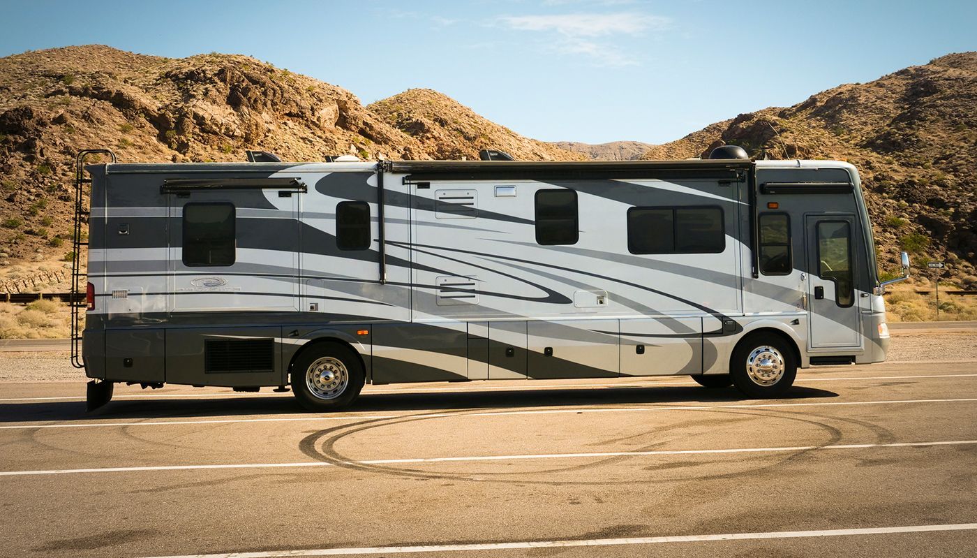 A large rv is parked in a parking lot with mountains in the background.