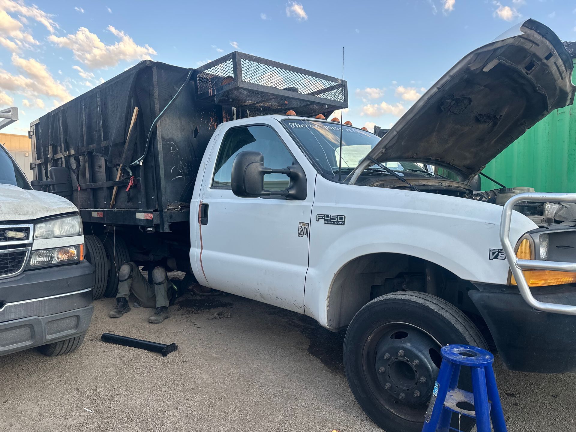 A white semi truck is being repaired in a garage with the hood up.