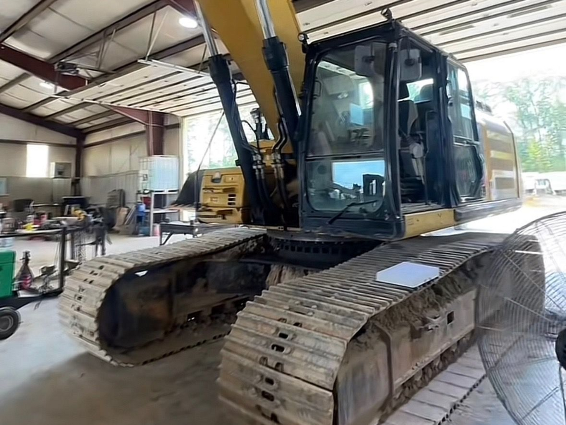 Yellow excavator inside a workshop with tracks.
