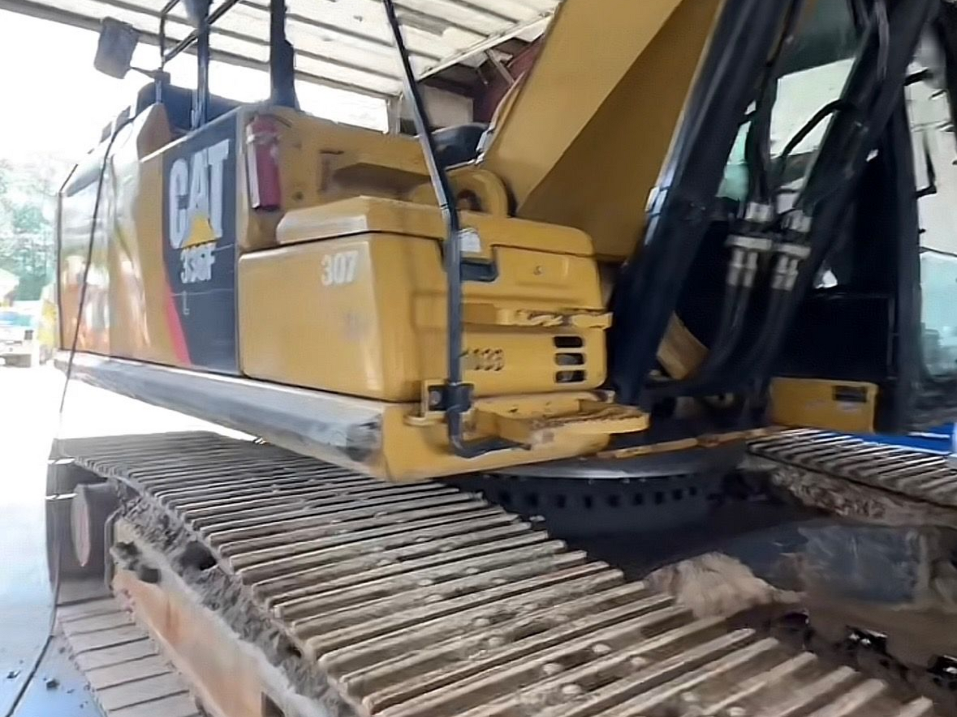 Yellow Caterpillar 307F excavator, track treads in foreground, parked in a bay.