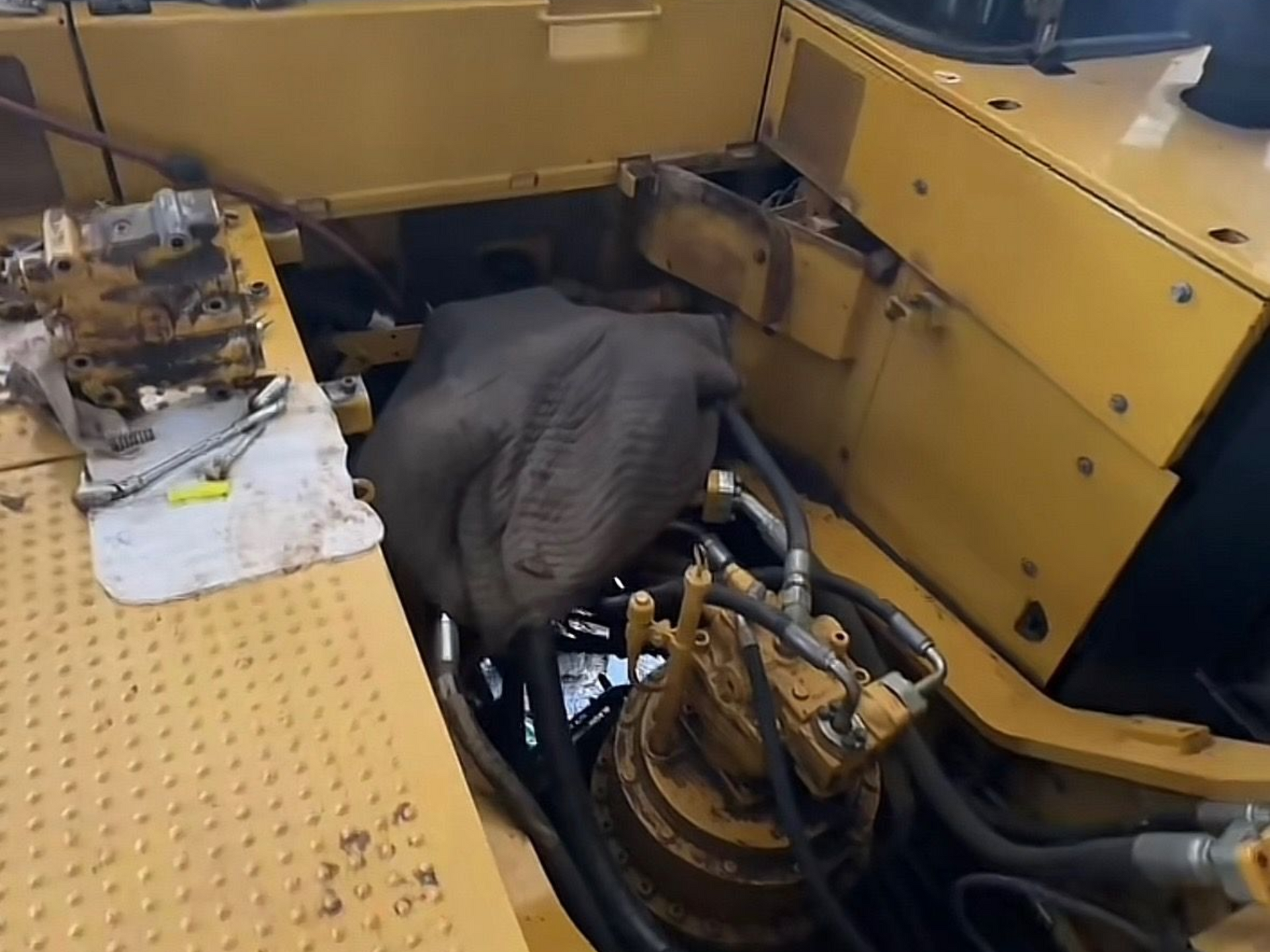 Interior of a yellow construction machine being worked on. Hydraulic lines and machinery are visible.