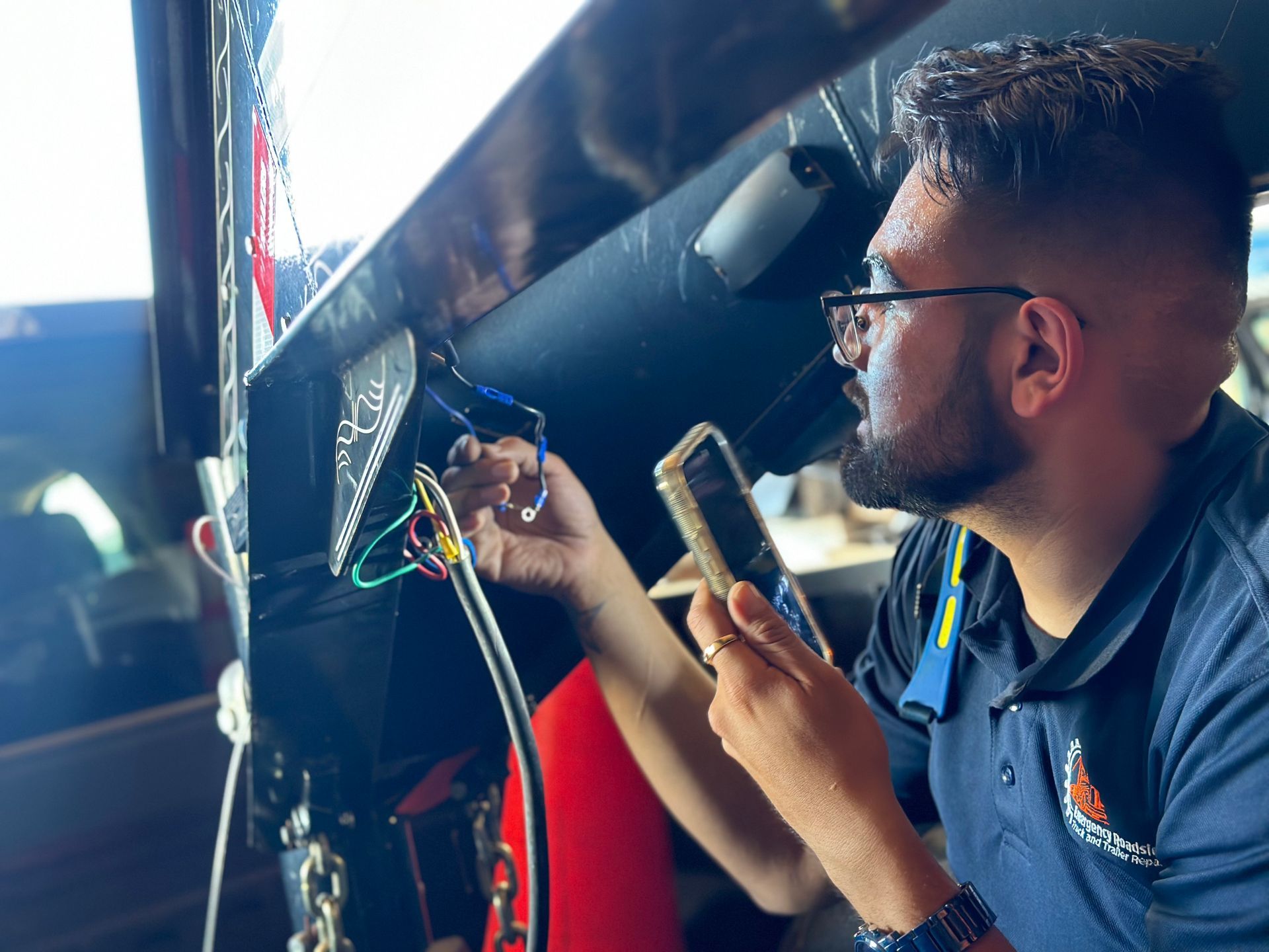 A man is working on a car while holding a cell phone.