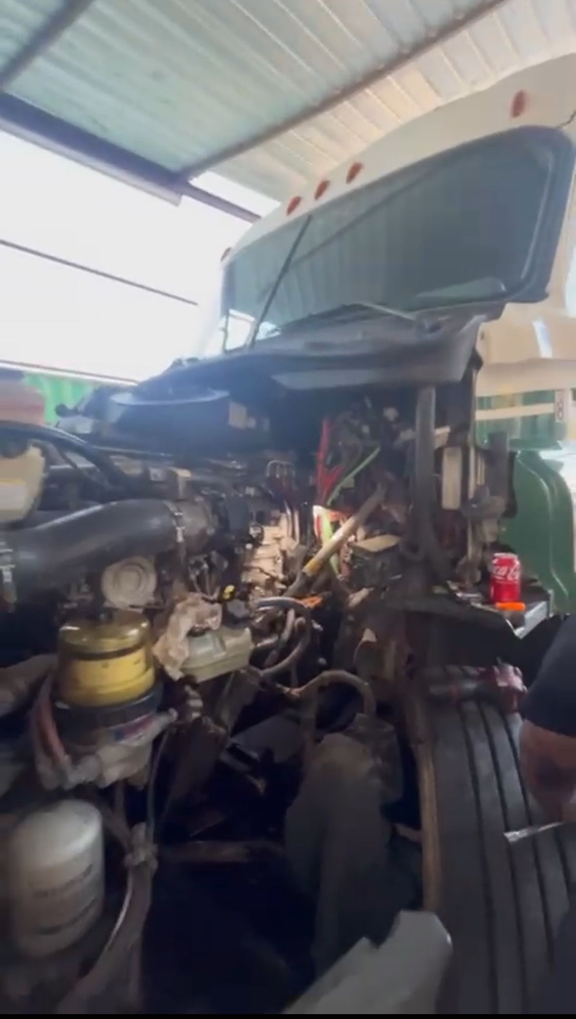 Truck engine bay with hood open, under repair. Numerous wires and parts visible. Sunlight shines in.