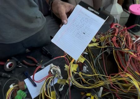 Person examining wiring diagram amidst a tangled bundle of colored wires. Tools and a notepad are nearby.