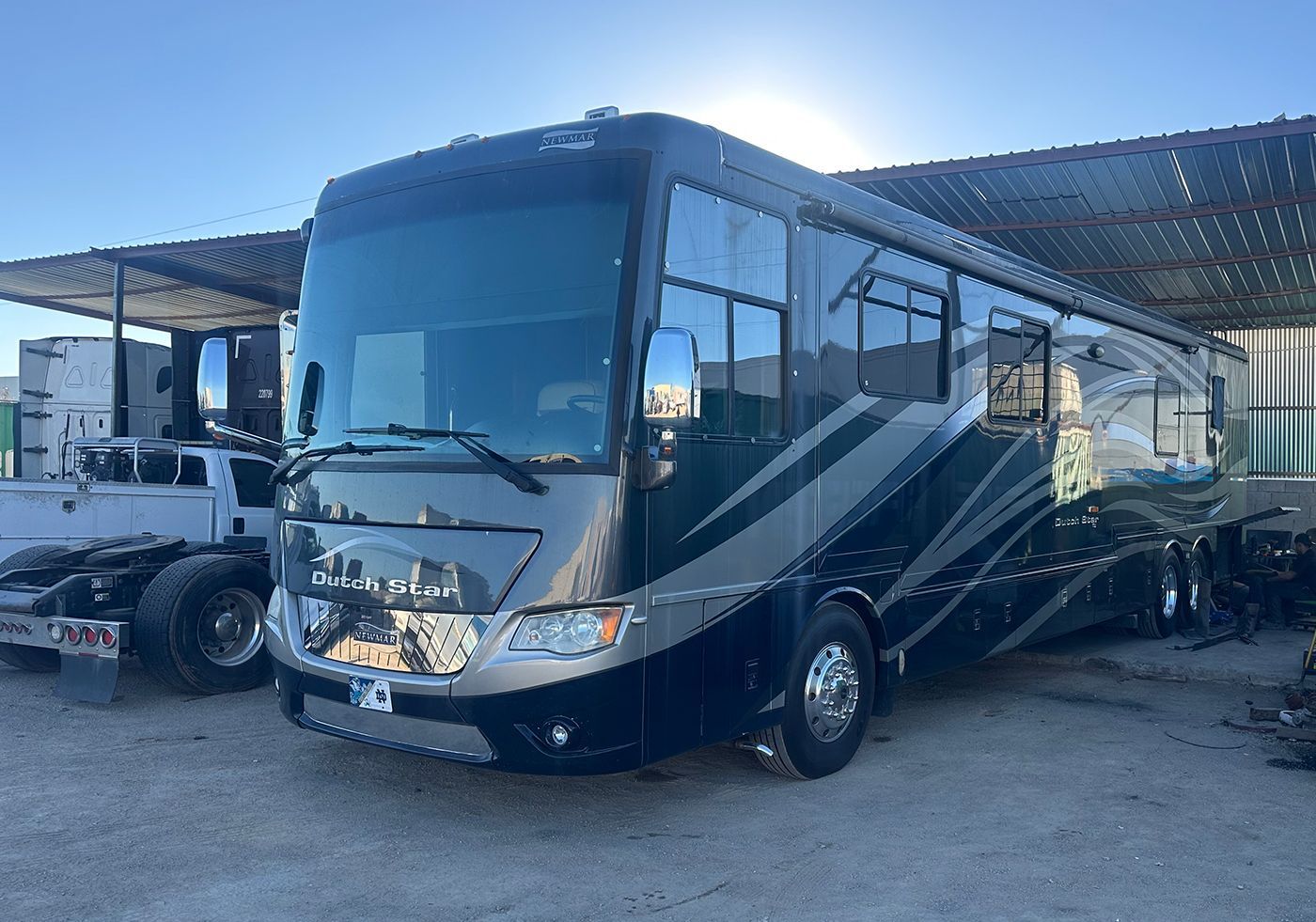 Large, dark-colored RV parked outside; gray and black exterior, multiple windows, parked in a lot.