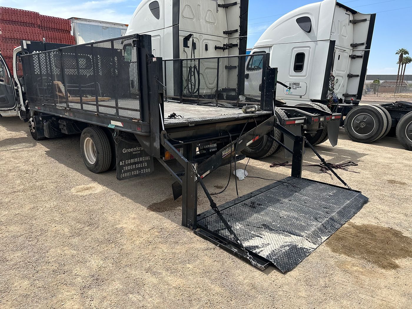 A truck with a ramp attached to the back of it is parked in a dirt field.