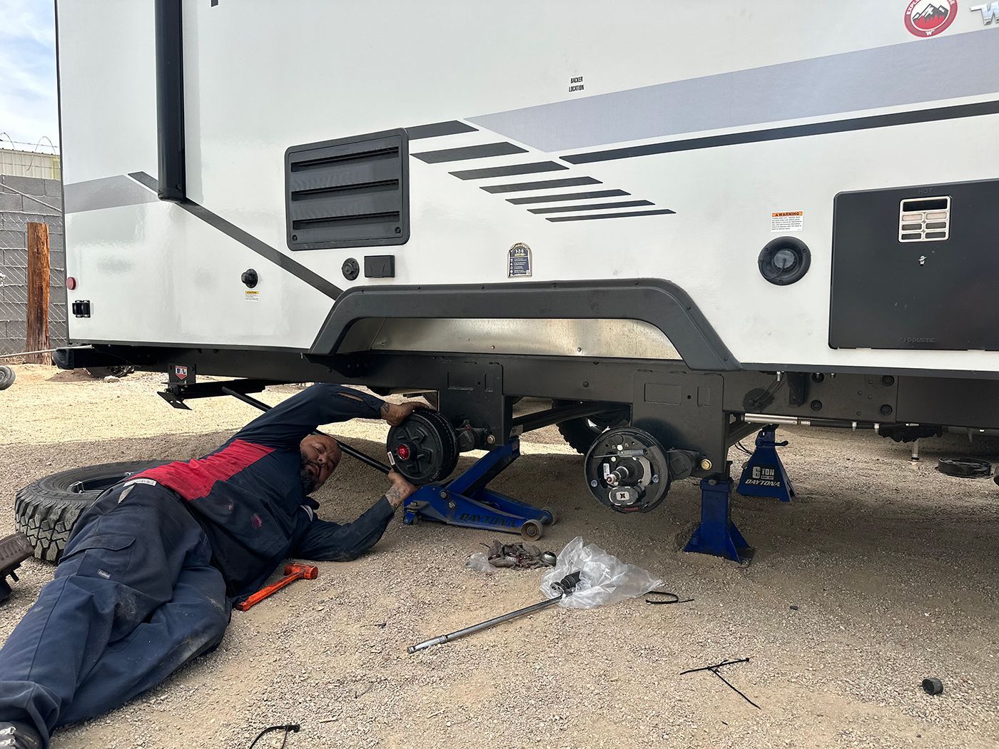 A man is laying on the ground working on a trailer.