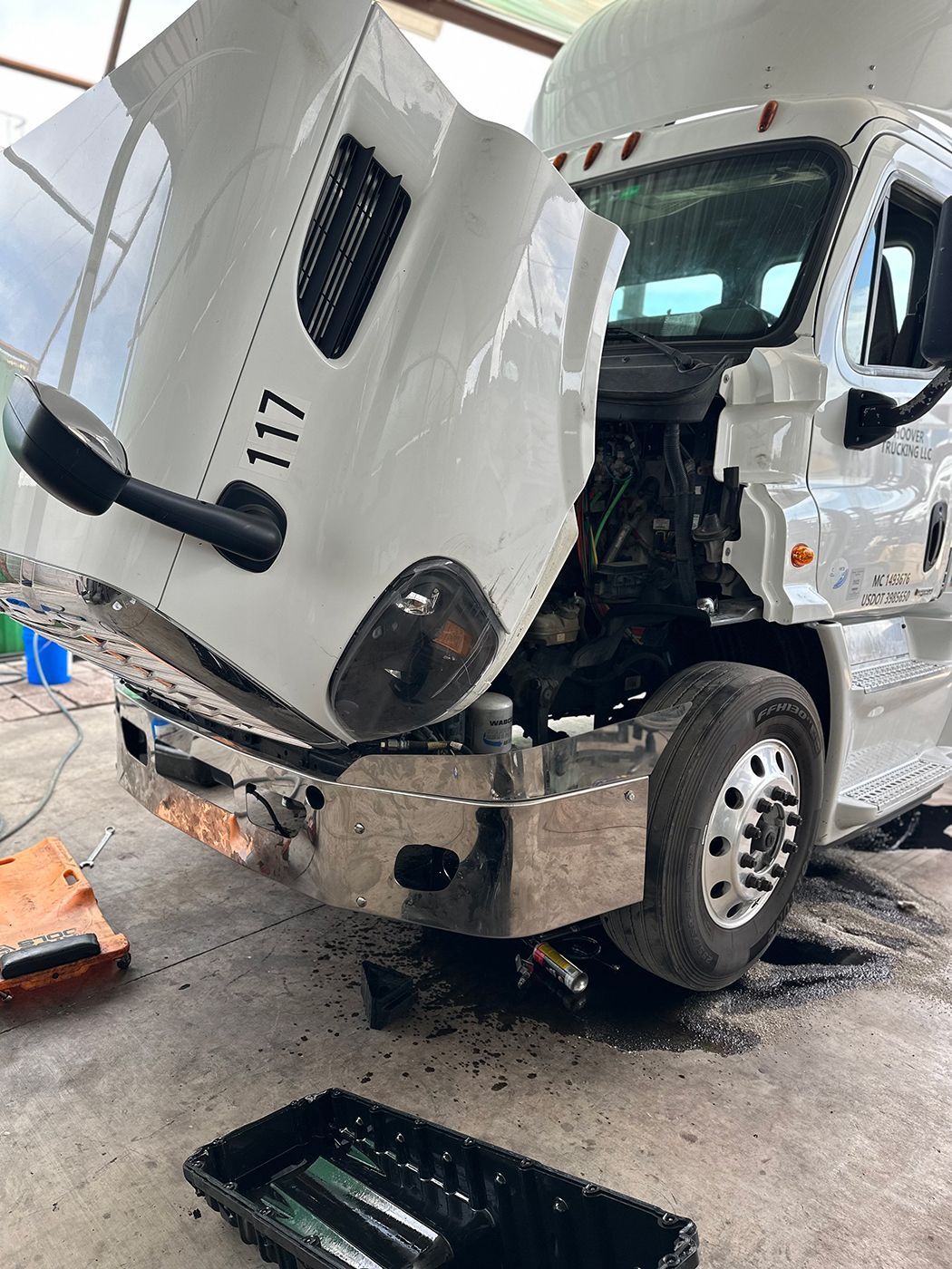 A white semi truck with its hood up is being repaired in a garage.