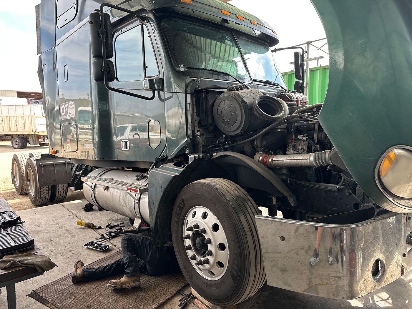 A semi truck is being repaired in a garage with the hood open.