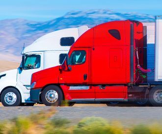 a red semi truck and a white semi truck are driving down a road .