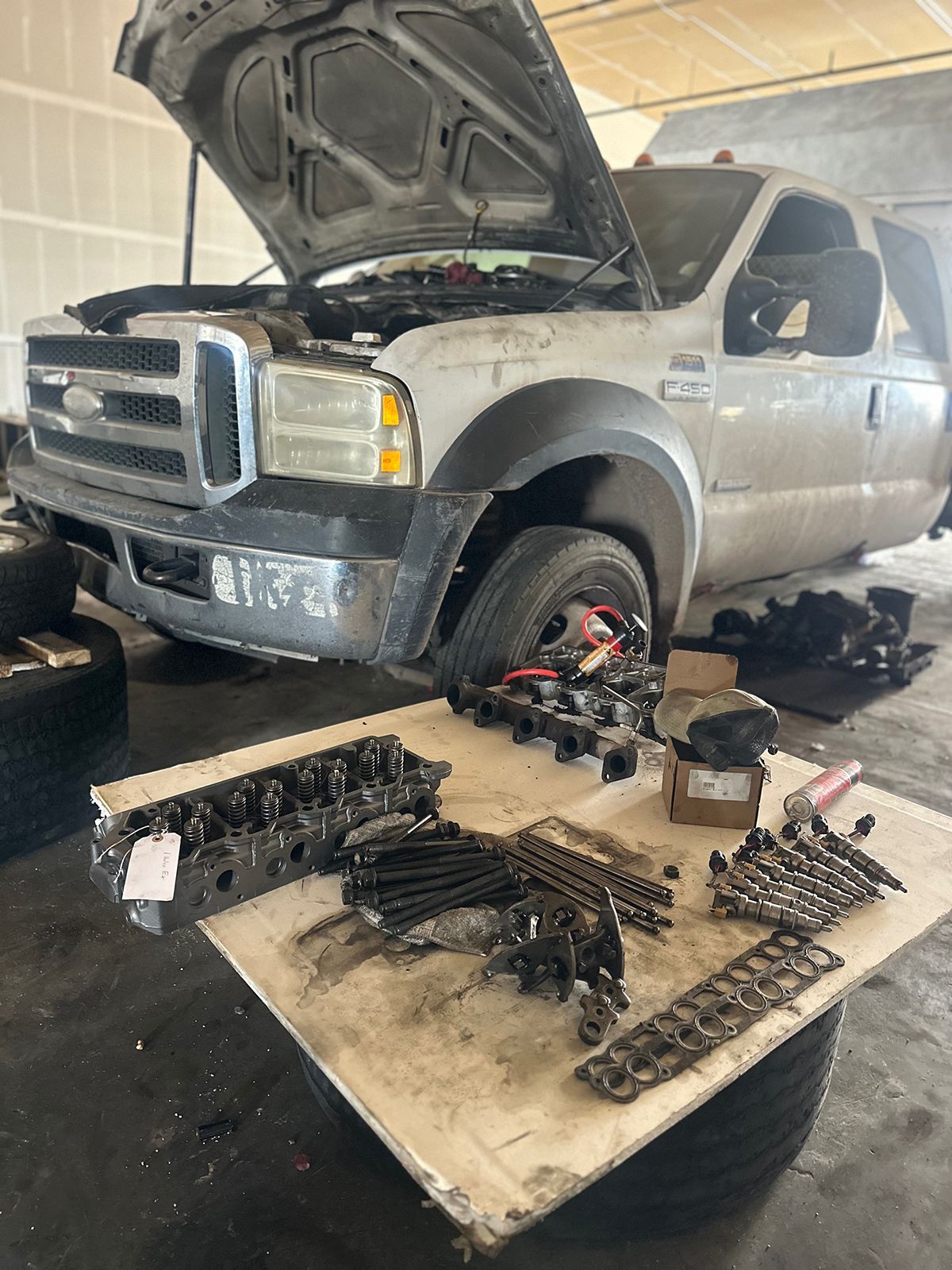 White Ford truck with hood open in a repair shop, engine parts on a table nearby.
