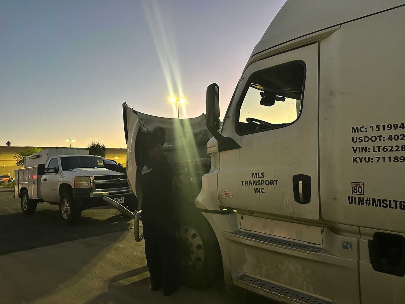 Truck with open hood being towed by a tow truck at sunrise.