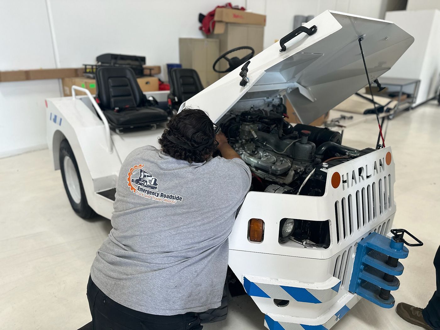 Woman working on a white and blue Harlan airport tug with the hood open.