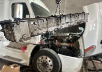 A truck is being repaired in a garage with the hood open.