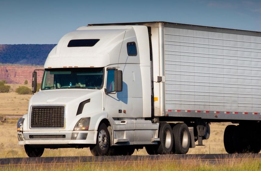 A white semi truck is driving down a road.