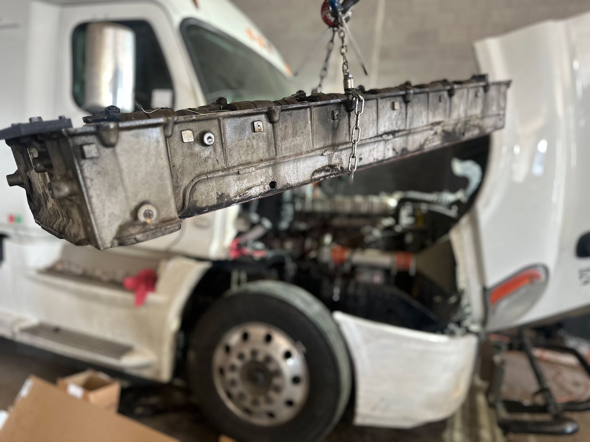 A white truck with the hood open is being worked on by a crane.