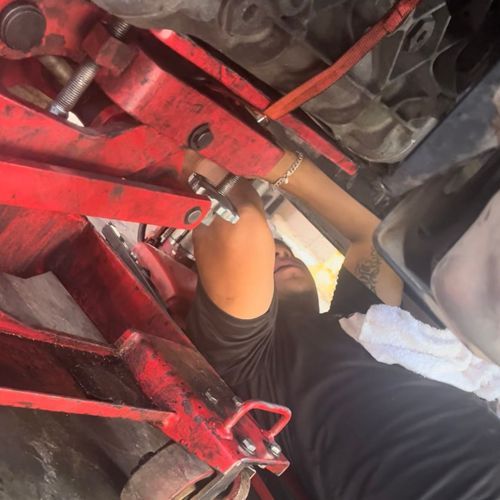 Person working under a car, using a red jack.