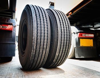 Two large truck tires, close-up, black rubber with tread pattern, on a gray surface.