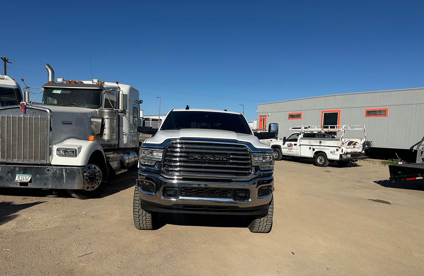 White Ram pickup truck parked in a gravel lot with other trucks and buildings under a blue sky.