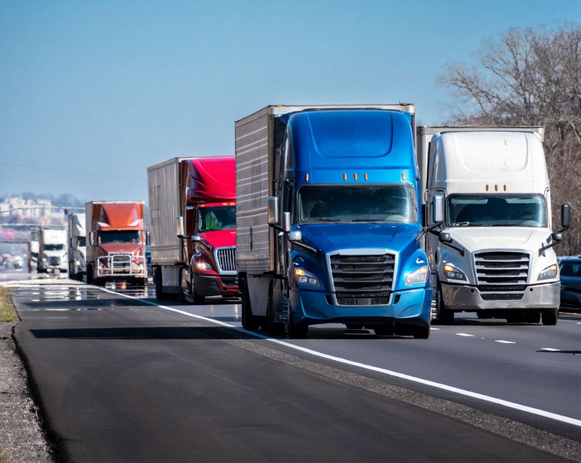 A row of semi trucks are driving down a highway.