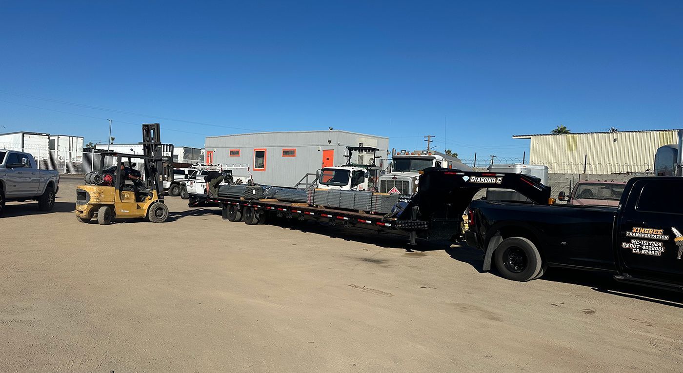 A forklift loading metal onto a trailer in a junkyard on a sunny day.