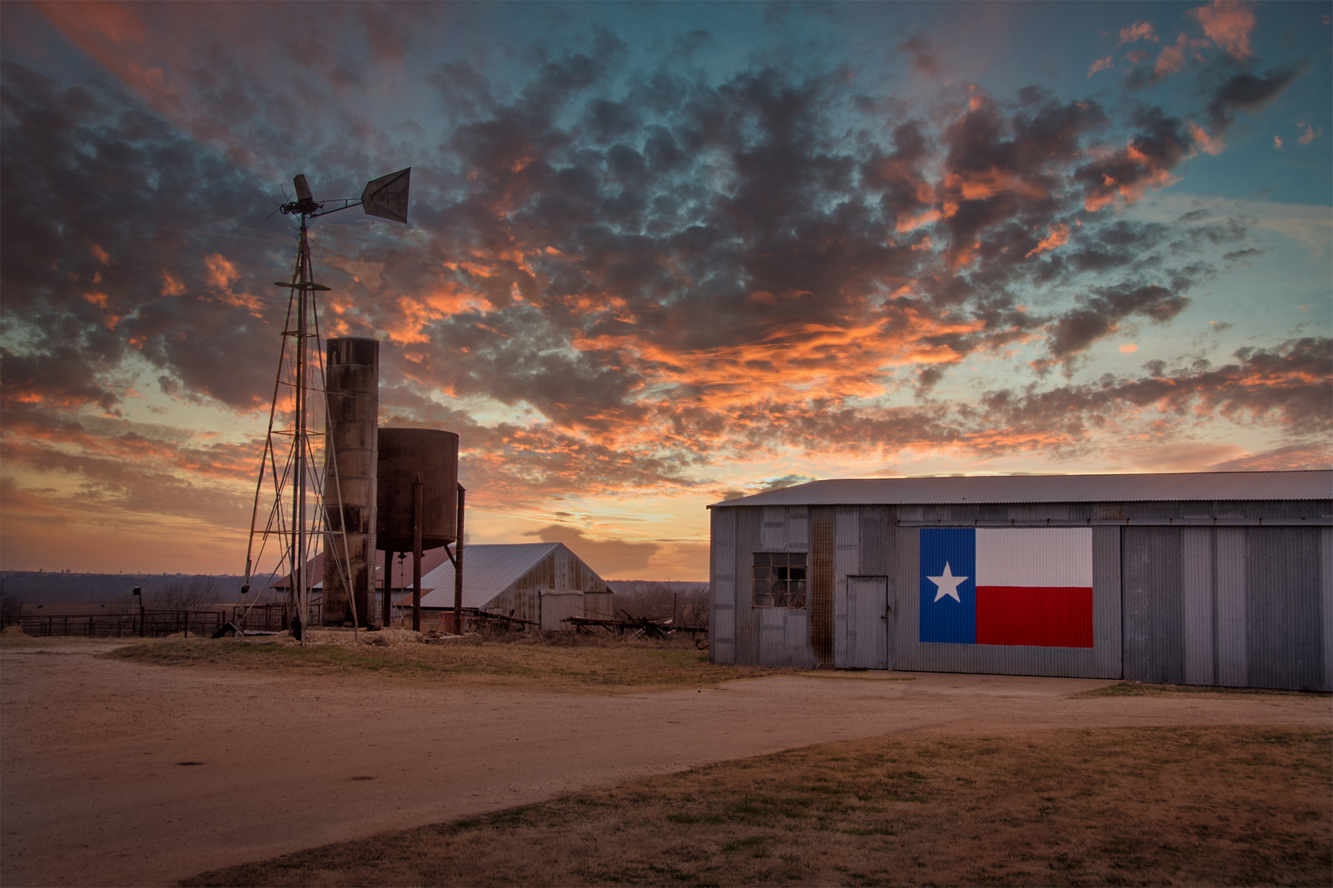 A barn with a texas flag painted on it and a windmill in the background.