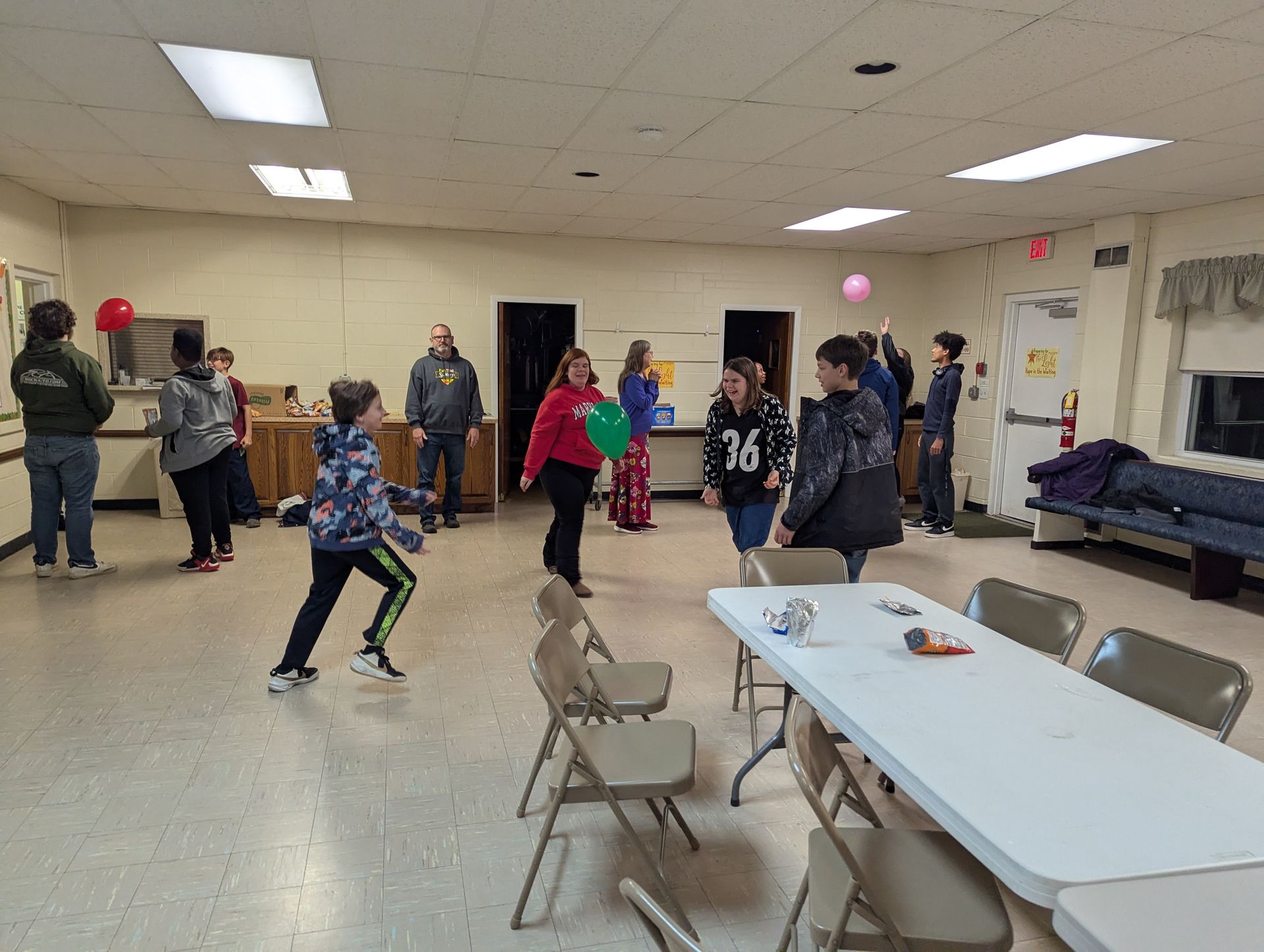 People in a room playing with balloons.  A child throws a ball, other people watch.