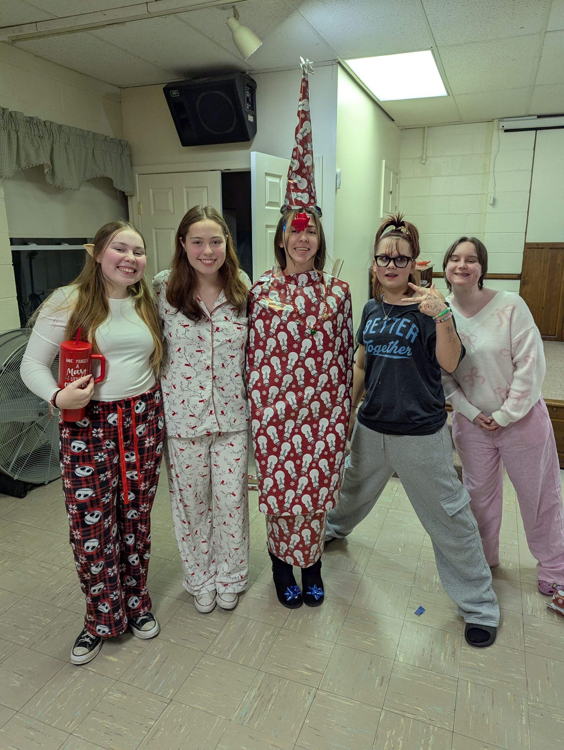 Five people in pajamas, one dressed as a Christmas tree, pose indoors.