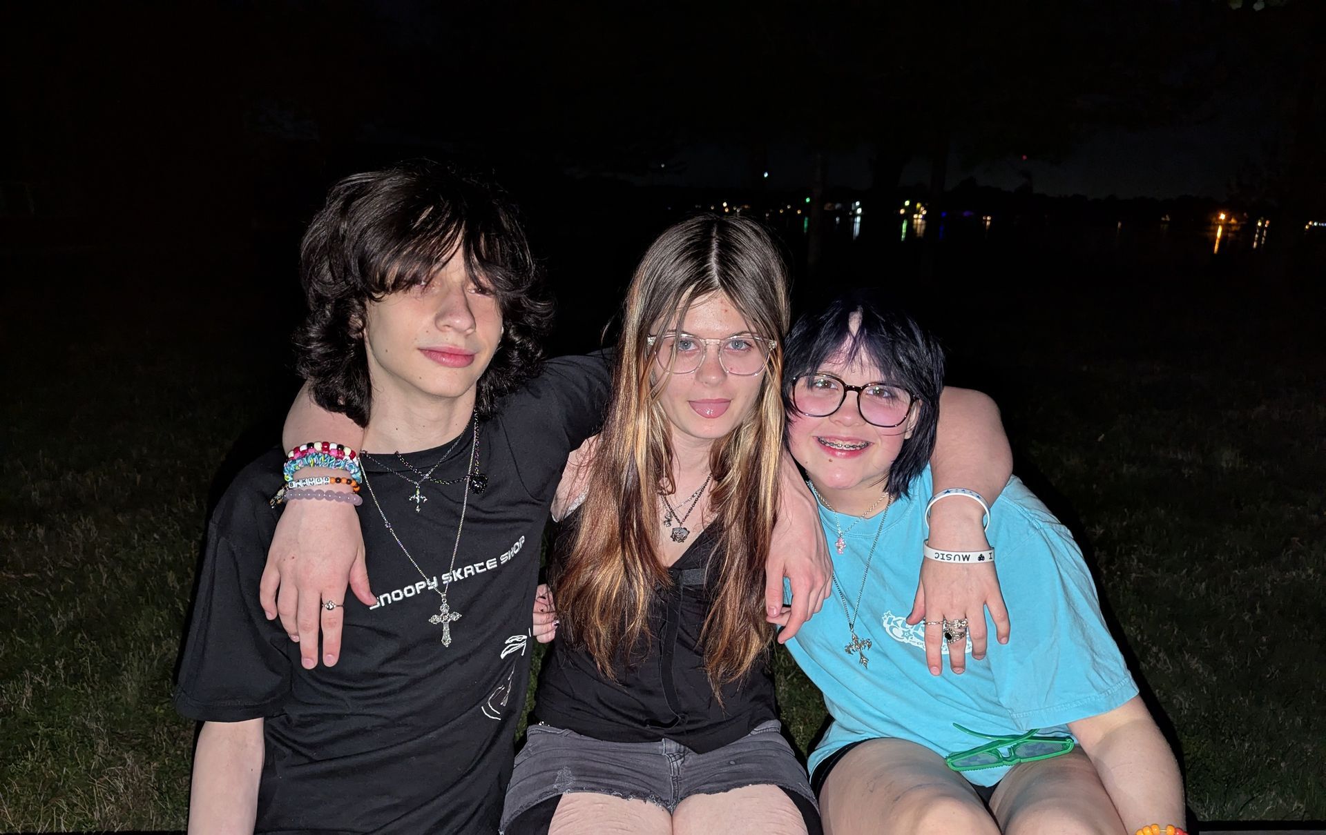 Three friends posing together at night, smiling with arms around each other