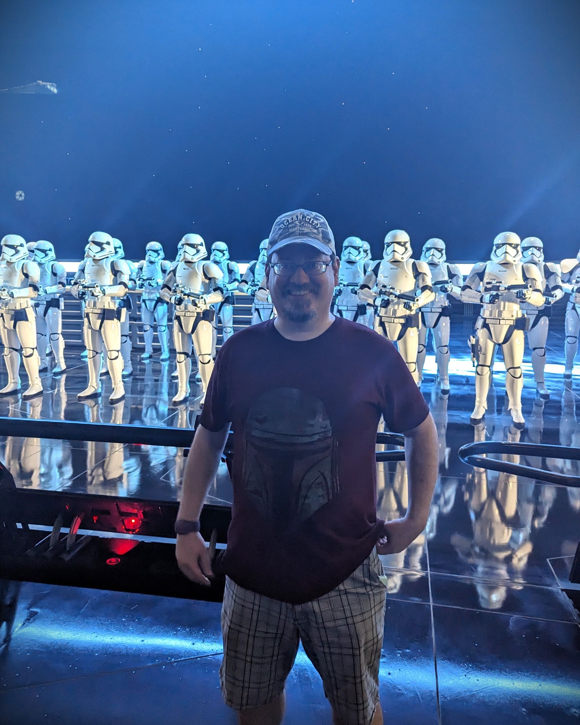 Man posing with Stormtroopers in a Star Wars ride setting; dark blue lighting.