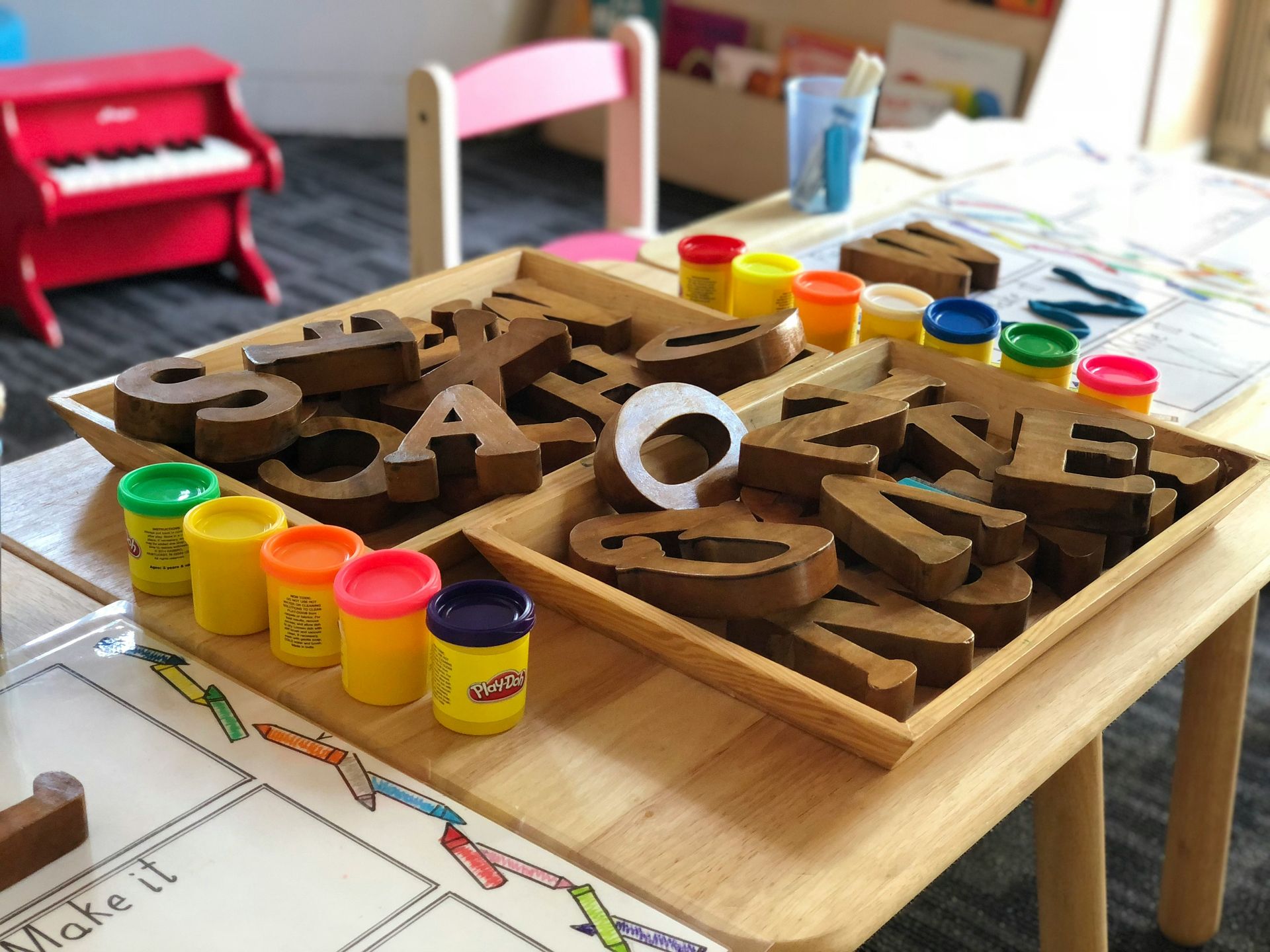 Wooden letters and playdough on a table in a classroom setting, promoting early learning activities.