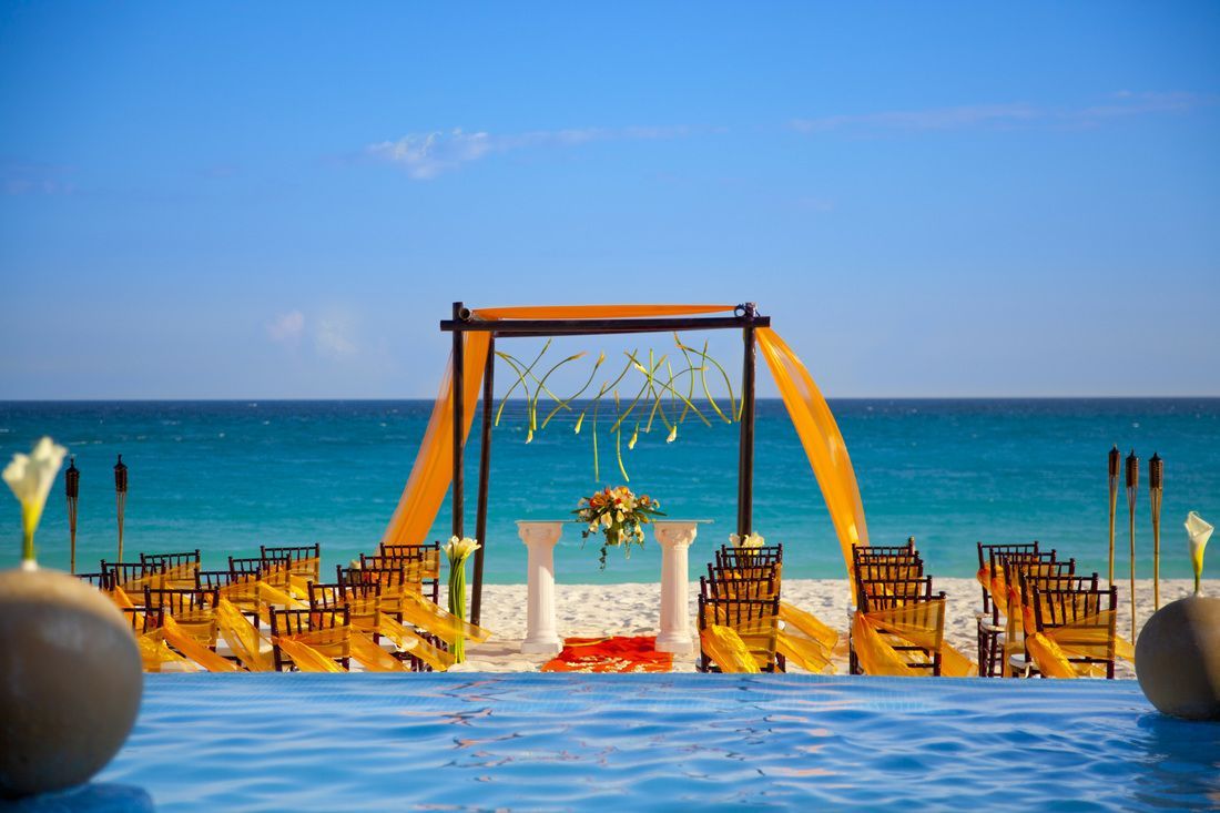 A wedding ceremony is set up on the beach near a swimming pool.