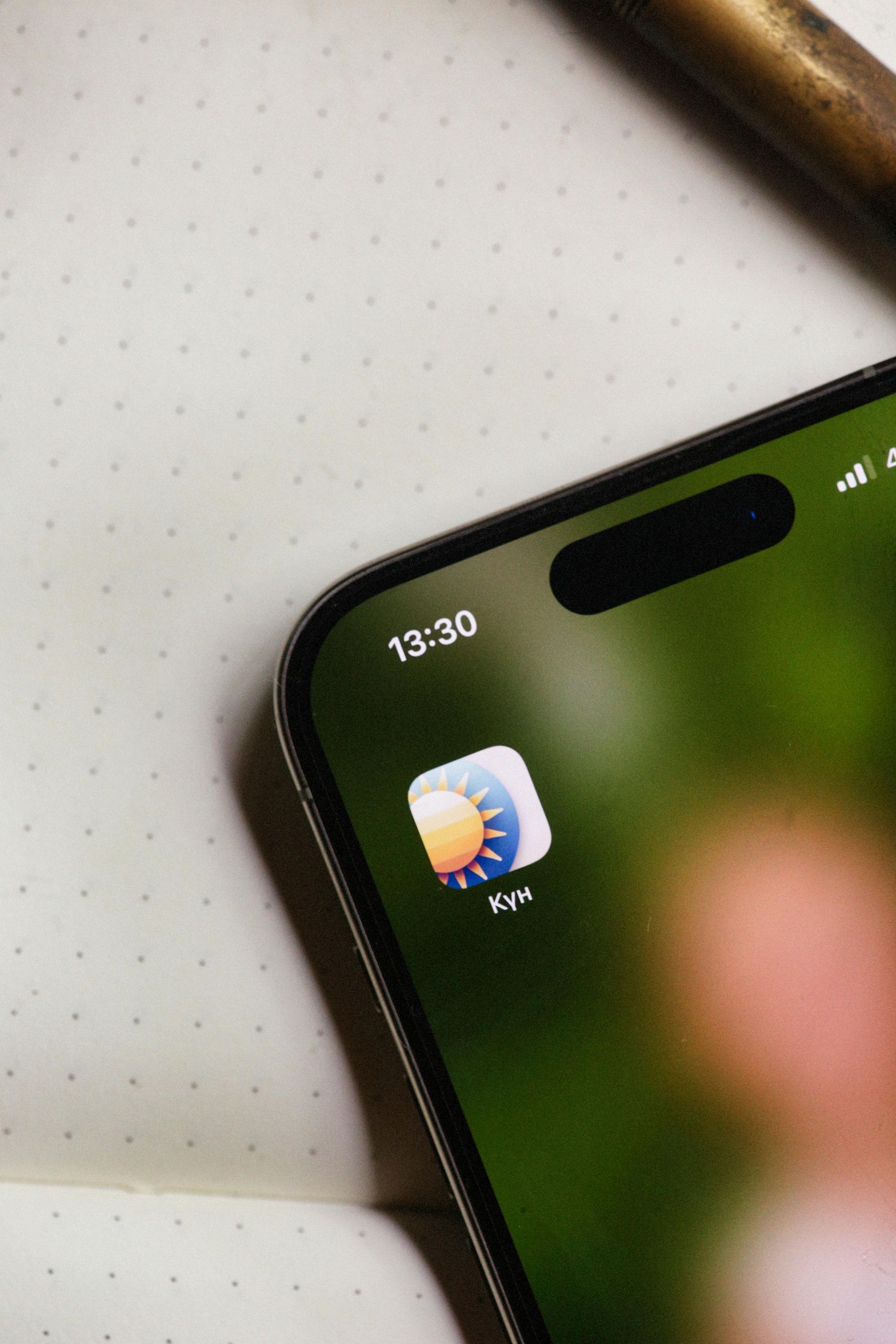 IPhone displaying a weather app icon on a green blurred background.
