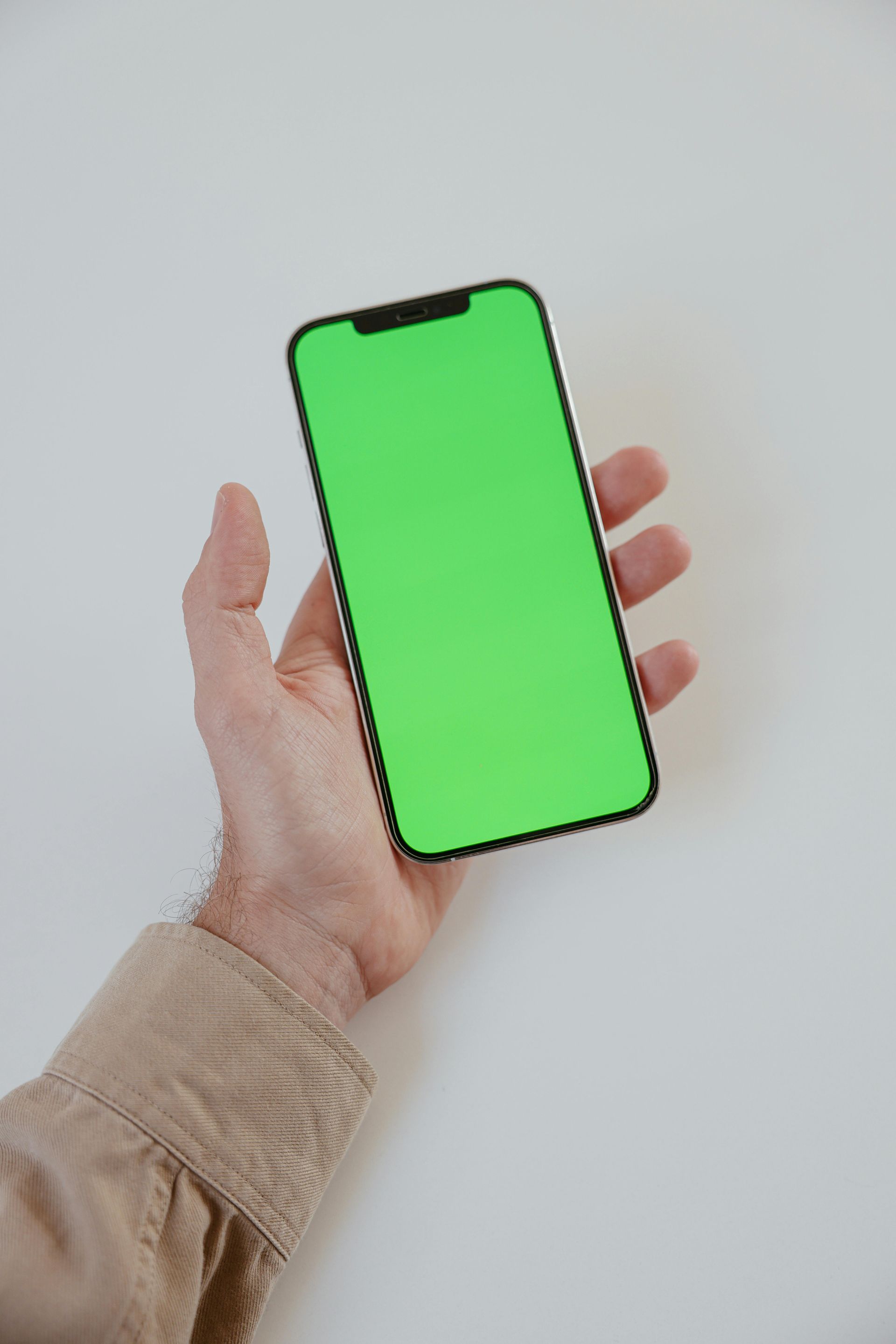Person's hand holding a smartphone with a green screen against a white background.
