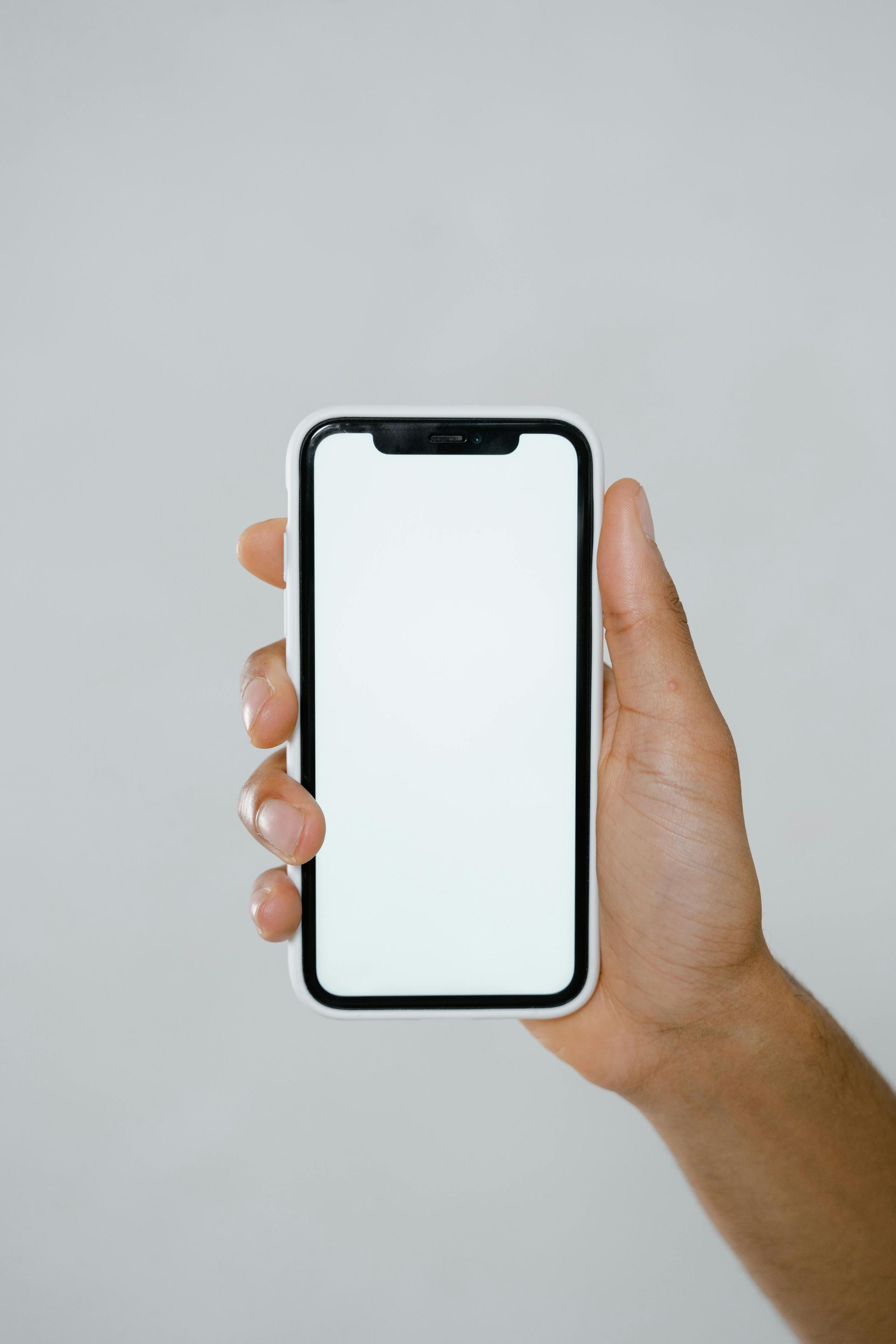 Hand holding a smartphone with blank white screen against a light gray background.